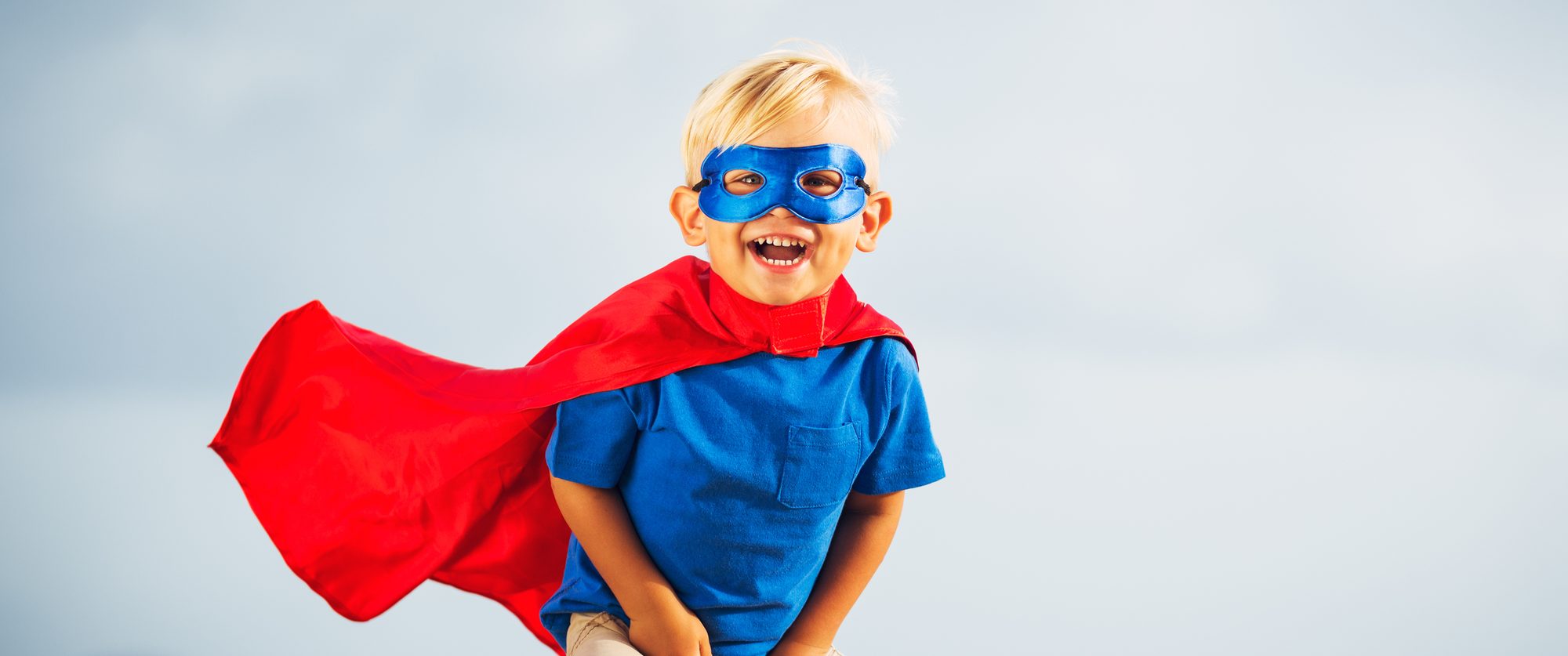 A smiling young boy in a superhero cape and mask
